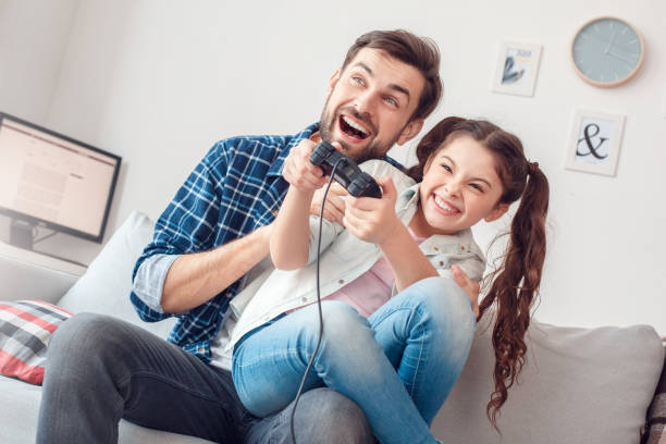 istock Father and little daughter at home sitting playing game console cheerful 1166511312