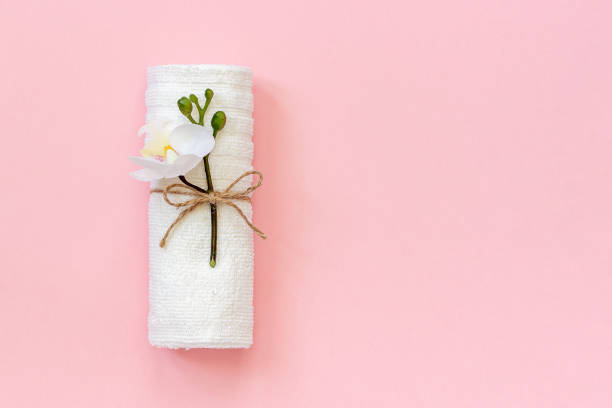 White towel roll tied with rope with sprig of orchid flower on pink paper background. Copy space Template for lettering text or your design stock photo