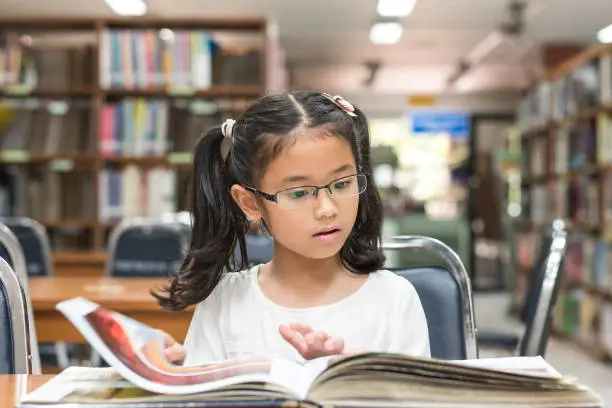 Photo of School education and literacy concept with Asian girl kid student learning and reading book in library or classroom