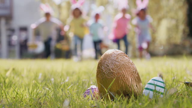 Group of children on Easter egg hunt running across garden towards chocolate egg - shot in slow motion