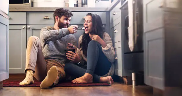 Shot of a happy young couple sharing a tub of ice cream in their kitchen at home