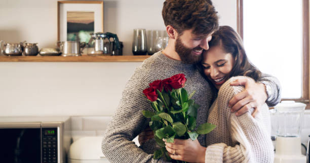 You don't need a reason to give her flowers Shot of a young man surprising his wife with a bunch of roses at home flowering plant stock pictures, royalty-free photos & images