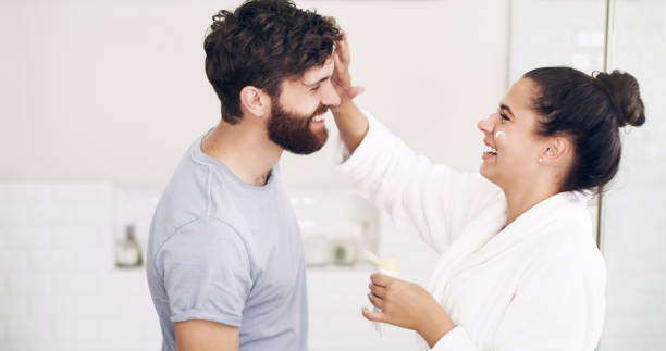 Trust me, I know the best beauty secrets Shot of a happy young woman applying moisturiser on her husband’s face during their morning grooming routine at home beauty treatment relaxation women carefree stock pictures, royalty-free photos & images