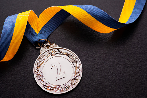 Second place runner-up silver medal on a twirled blue and gold ribbon over a dark grey background with copy space viewed from above
