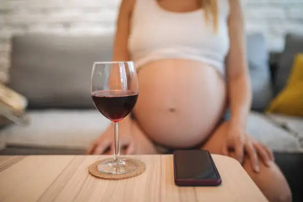 Pregnant woman sitting and thinking about beating her alcohol addiction