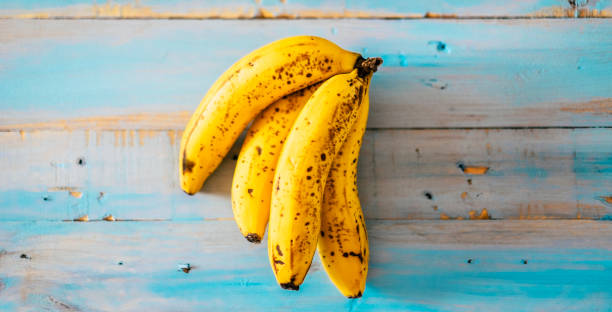 gelbe bananen auf einem blauen holztisch hintergrund - konzept von kalium und gesundem lebensstil mit saisonalen früchten - vitamine und vegetarische oder vegane lebensweise für gesunde menschen - banana bunch yellow healthy lifestyle stock-fotos und bilder