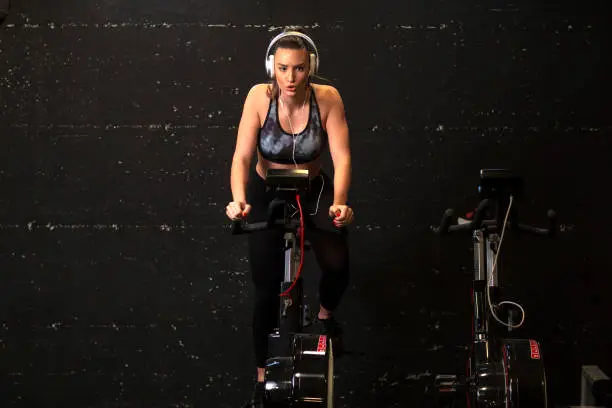 Woman exercise in gym on bike and liste music over headphones on her head