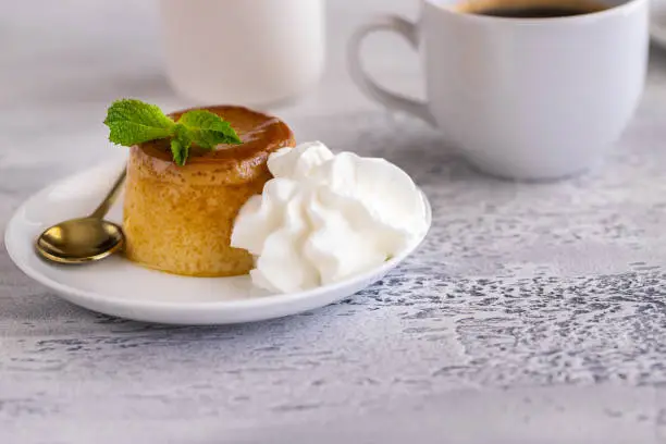 Photo of Creme caramel dessert or flan  decorated  with whipped cream and mint  and served with cup of coffee. Sweet moment background.