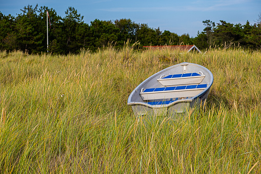 A rowboat rests in the grassy field on a beach in Denmark. The beach is near the city of Hojby.