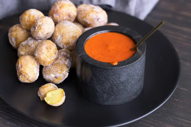 Photo of Famous Canary Islands dish, Papas Arrugadas (wrinkly potatoes with salt) and Mojo picon (red sauce) on wood table