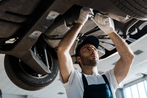 low angle view of serious car mechanic repairing automobile in car service low angle view of serious car mechanic repairing automobile in car service wheel cap stock pictures, royalty-free photos & images