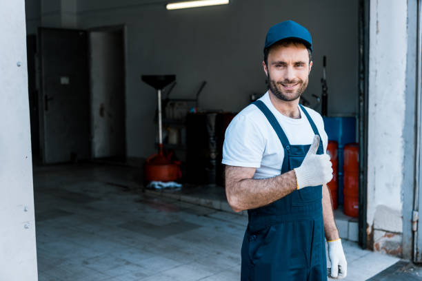 istock handsome bearded car mechanic in cap standing and showing thumb up 1166557132