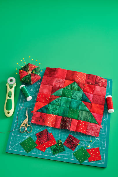 istock Christmas tree patchwork block, bright square pieces of fabric, pincushion, quilting and sewing accessories on craft mat, green background 1166557381