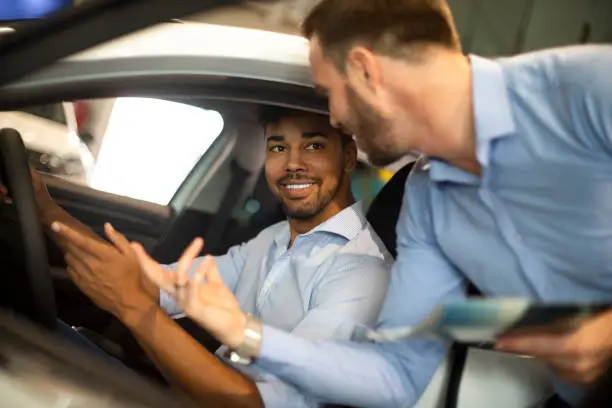 Car salesperson showing the new car model features to a customer in an automotive dealership.