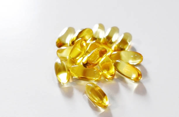 istock Transparent yellow oblong capsules with fish oil (omega 3), which are scattered on a white table 1166559441