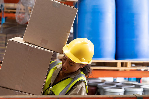 Side view of female staff carrying cardboard boxes in warehouse. This is a freight transportation and distribution warehouse. Industrial and industrial workers concept