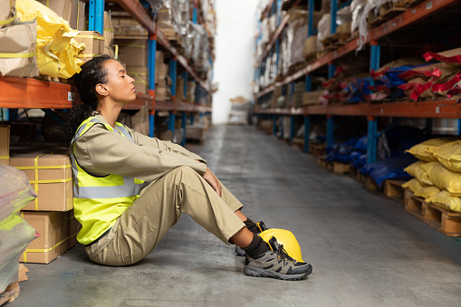 Tired female staff sitting with eyes closed in warehouse. This is a freight transportation and distribution warehouse. Industrial and industrial workers concept