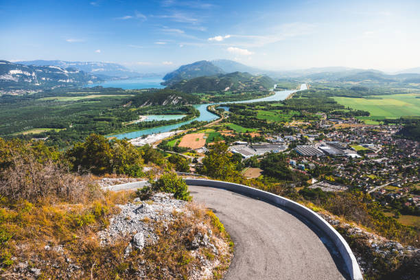 fermez-vous près de la route sinueuse de montagne sur le sommet de grand colombier, français paysage au milieu des montagnes de bugey dans le département de l'ain, avec la petite ville de culoz, la rivière du rhône et le célèbre lac bourget en été - winding road sunlight field cultivated land photos et images de collection