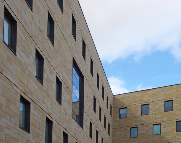 a corner view of a modern stone building with geometric repeating pattern of small windows and blue sky