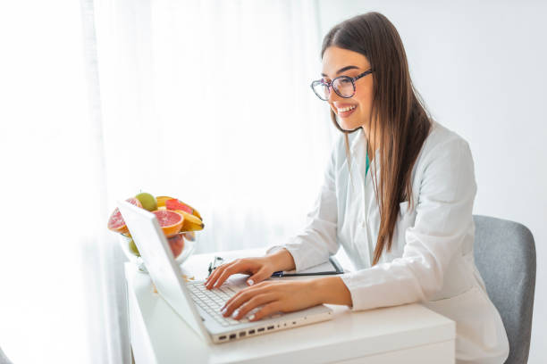 retrato de hermosa nutricionista sonriente mirando a la cámara y mostrando verduras saludables en la consulta. - healthy eating red colors healthcare and medicine fotografías e imágenes de stock