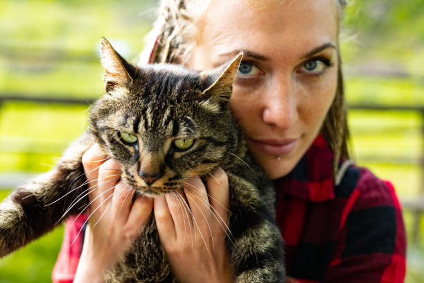Attractive serious young woman holding her cat to her chest for a portrait together outdoors in the garden