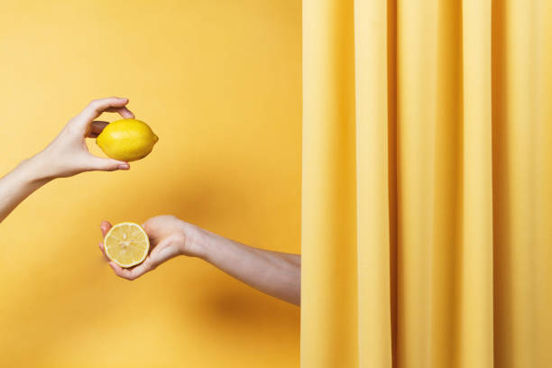 istock Two women's hands holding cut and whole lemons on yellow 1166575414