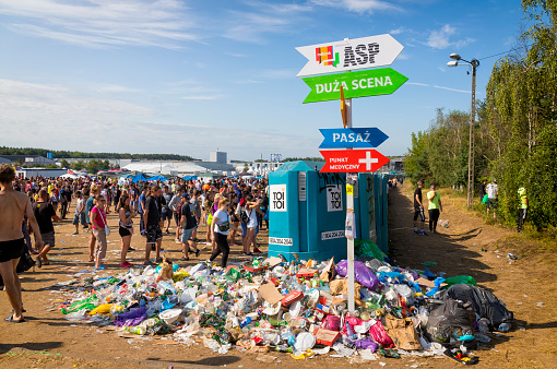 Kostrzyn Nad Odra, Poland - August 03, 2019:Festival signpost and portable toilets with garbage and a large crowd of young people. The 25th Pol'and'rock Festival - the biggest open air ticket free rock music festival in Europe
