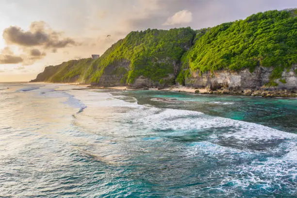 Sunset scene - blue ocean and cliffs, covered with tropical plants. Aerial view of the Melasti beach, Bali