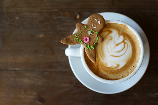 A cup of latte with a gingerbread cookie on elegant dark brown background. Closeup view. Cozy winter holidays composition.