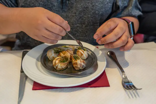 Woman hand using small fork eating Escargots de Bourgogne