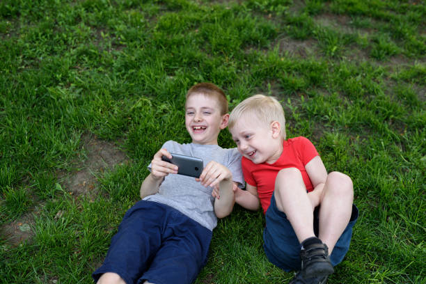 Two boys with a smartphone in their hands having fun on the grass