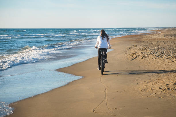istock Woman rides a Bicycle along the sea on a sandy beach. Back view. 1166583421