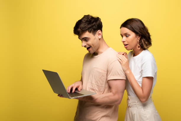 istock smiling young man using laptop while standing near pretty girl on yellow background 1166584265