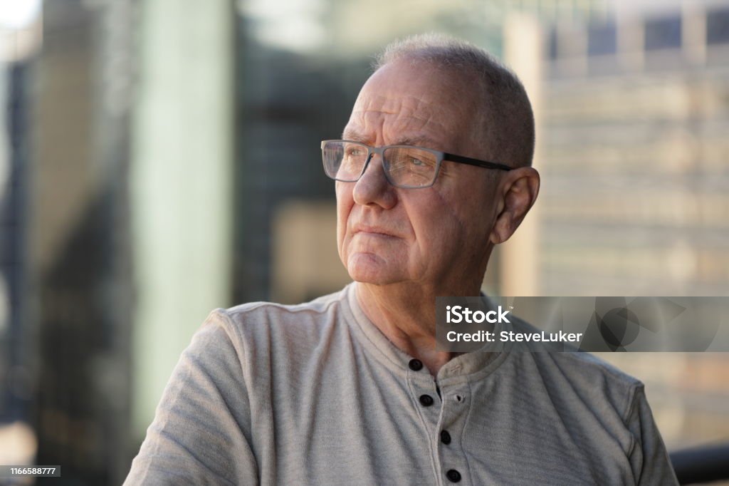 Senior man remembering Senior man with facial scar looking to the side. Out of focus office buildings in the background. Men Stock Photo
