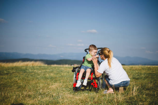 Mother crouching by son in wheelchair at field stock photo