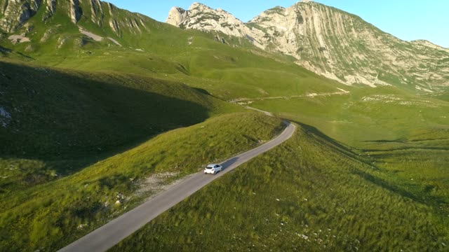 Aerial view of white car driving on mountain serpentine road in sunset lights. Aerial 4K drone shot