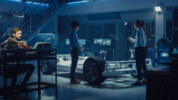 istock Automotive Design Engineers Talking while Working on Electric Car Chassis Prototype. In Innovation Laboratory Facility Concept Vehicle Frame Includes Wheels, Suspension, Engine and Battery. 1166604608