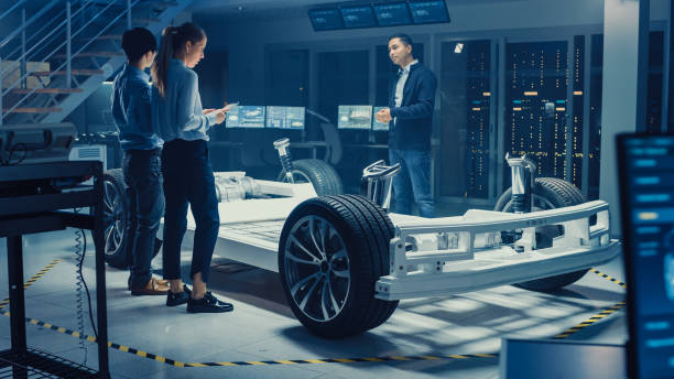 istock Automotive Design Engineers Talking while Working on Electric Car Chassis Prototype. In Innovation Laboratory Facility Concept Vehicle Frame Includes Wheels, Suspension, Engine and Battery. 1166604638