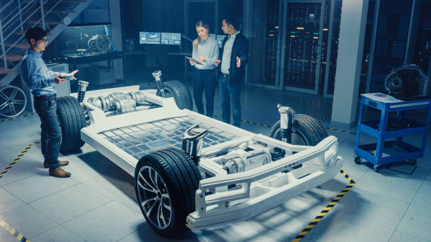 istock High Angle Shot of a Development Laboratory Room with Diverse Professional Team of Engineers and Scientists Working on a Electric Car Chassis with Wheels, Batteries, Engine and Suspension. 1166604659