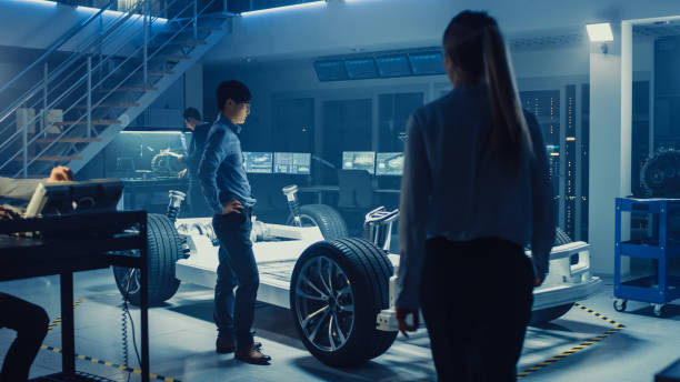 istock Development Laboratory Room with Diverse Professional Team of Engineers and Scientists Working on a Electric Car Chassis with Wheels, Batteries, Engine and Suspension. 1166604667