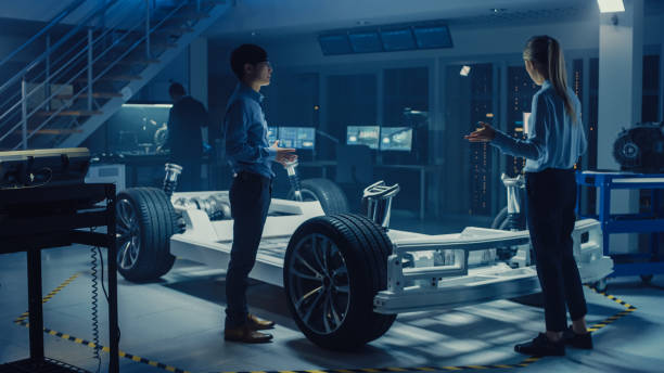 istock Automotive Design Engineers Talking while Working on Electric Car Chassis Prototype. In Innovation Laboratory Facility Concept Vehicle Frame Includes Wheels, Suspension, Engine and Battery. 1166604672