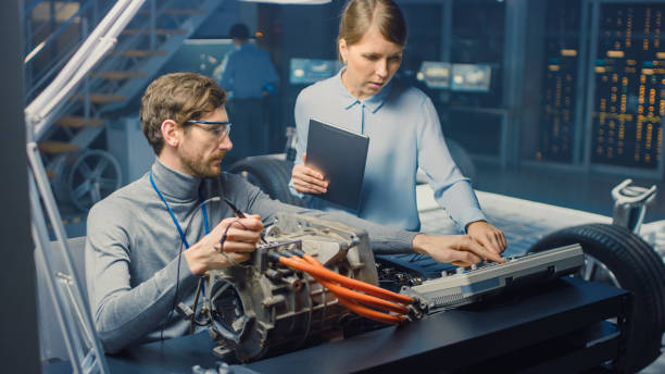 Male and Female Automotive Engineers with a Tablet Computer and Inspection Tools are Having a Conversation While Testing an Electric Engine in a High Tech Laboratory with a Concept Car Chassis. ingenieros de automoción masculinos y femeninos con una tableta informática y herramientas de inspección están teniendo una conversación mientras prueban un motor eléctrico en un laboratorio de alta tecnología con un chasis de coche conceptual.