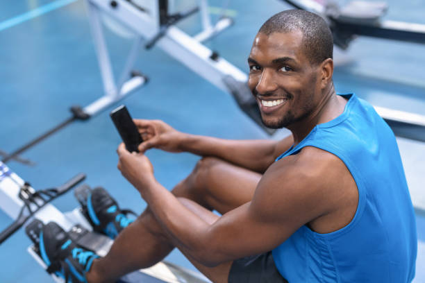 istock Fit man using mobile phone while exercising on rowing machine in fitness center 1166605861