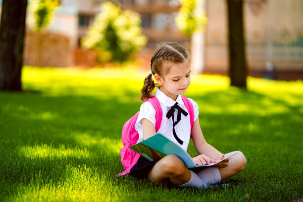 istock Little school girl with pink backpack sitting on grass after lessons and read book or study lessons, thinking ideas, education and learning concept 1166607889