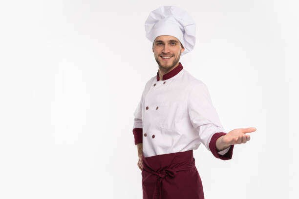 istock Image of smiling young cook in uniform standing isolated over white background. Looking camera pointing. 1166608412
