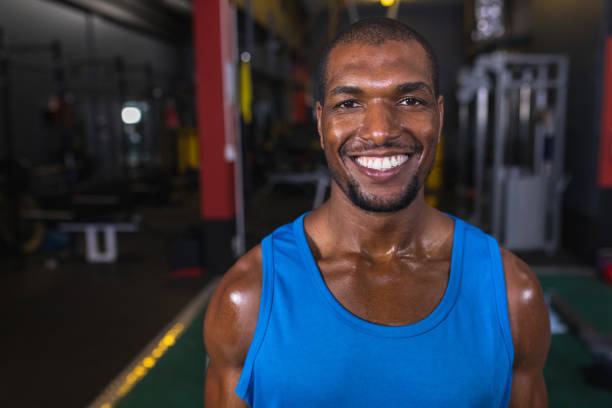 Close-up of African-american male athletic looking at camera while standing in fitness center. Bright modern gym with fit healthy people working out and training