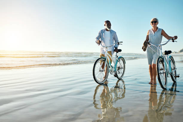 quand c'est l'été, tu dois faire un tour sur la plage - senior couple cycling beach bicycle photos et images de collection