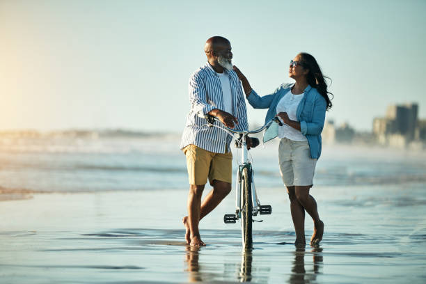 règle numéro un, n'oubliez pas de vous amuser - senior couple cycling beach bicycle photos et images de collection