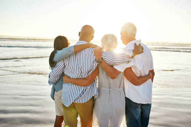 They got the best gift of all, friendship Rearview shot of a group of senior friends embracing at the beach black couple sunset stock pictures, royalty-free photos & images