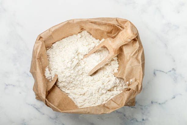 wheat flour and a wooden scoop in a paper bag on a marble table. bakery concept. selective focus - ground flour white heap imagens e fotografias de stock